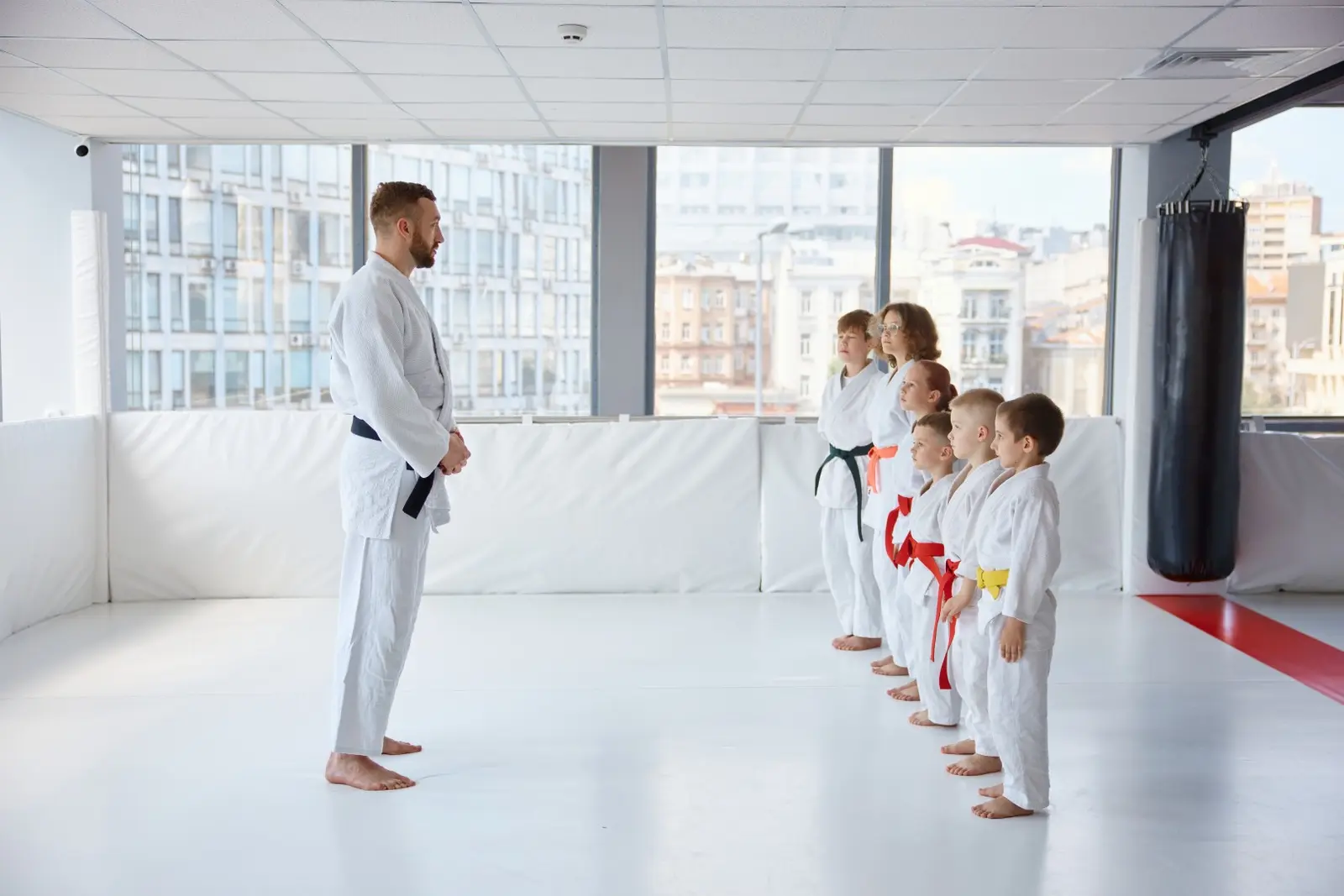 Sensei en ceinture noire face à une rangée d'enfants en kimono blanc sur le tatami avant un entraînement d'arts martiaux